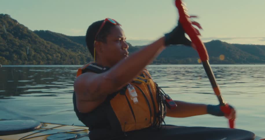 Concentrated woman using paddle in a canoe on a calm river with mountains in the background