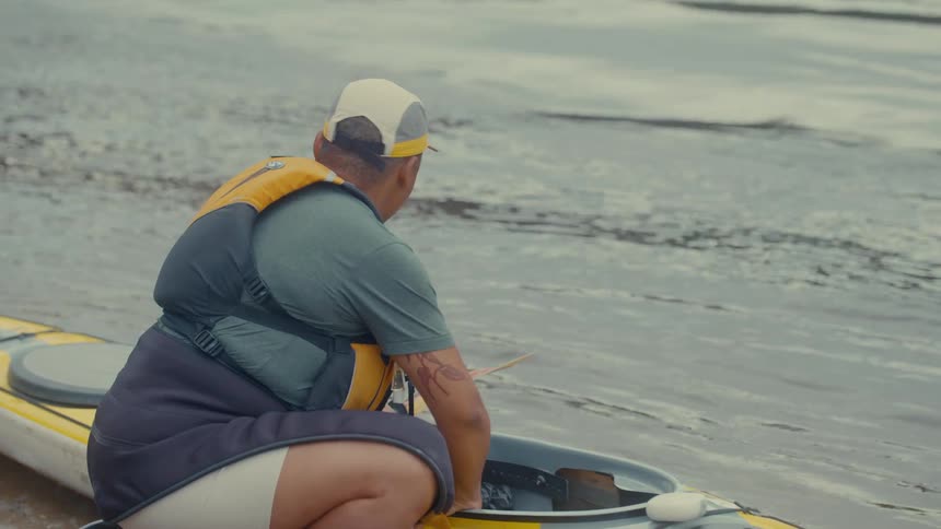 Man crouches near his kayak as it floats on the water