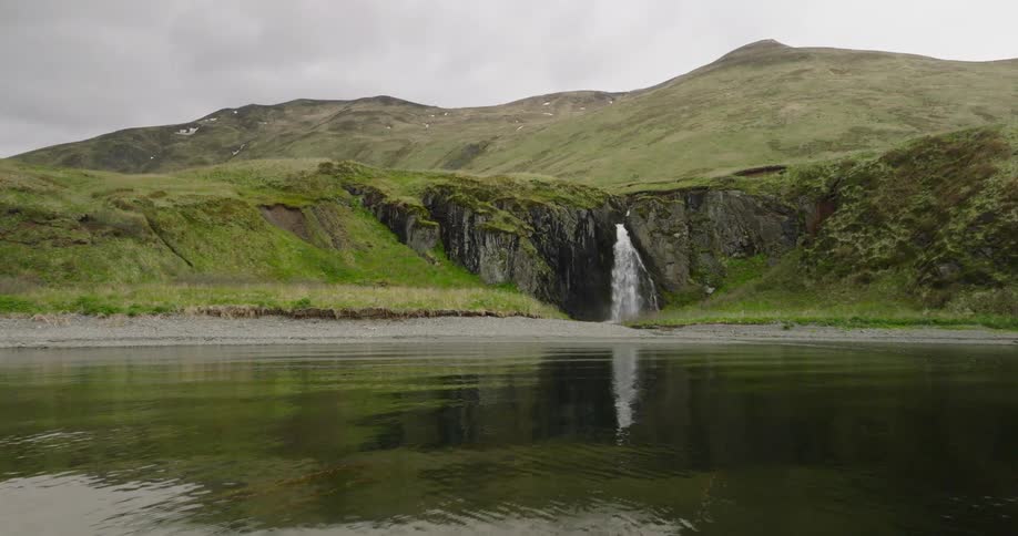 A waterfall tumbles over the mossy cliffside its water crashing into the bay below