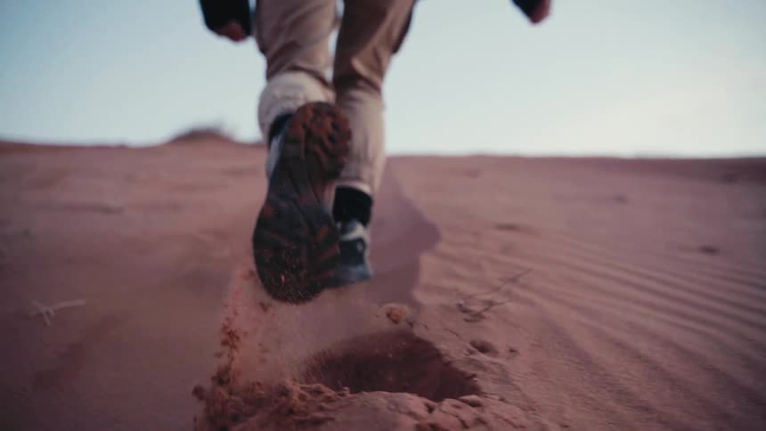 A hiker walks up a sand dune in a desert
