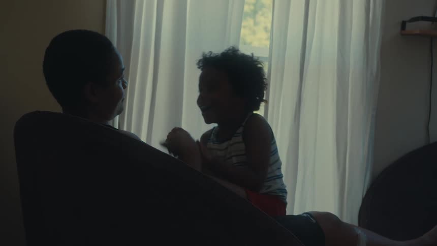 Father sitting in an armchair with his son on top and they both play