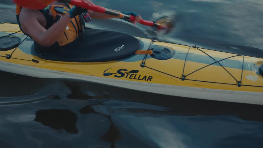 A person wearing a life vest paddles a yellow stellar kayak through dark rippled water