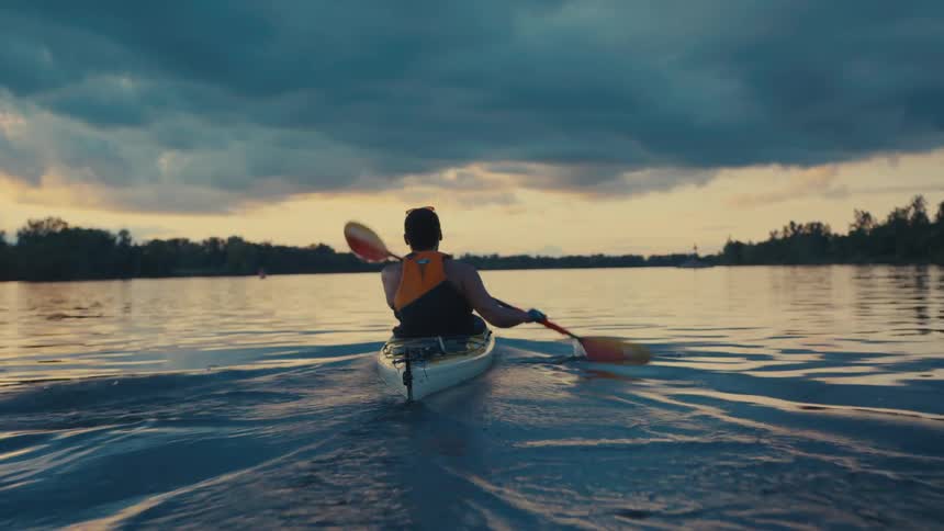 A man is paddling in the kayak on the large lake