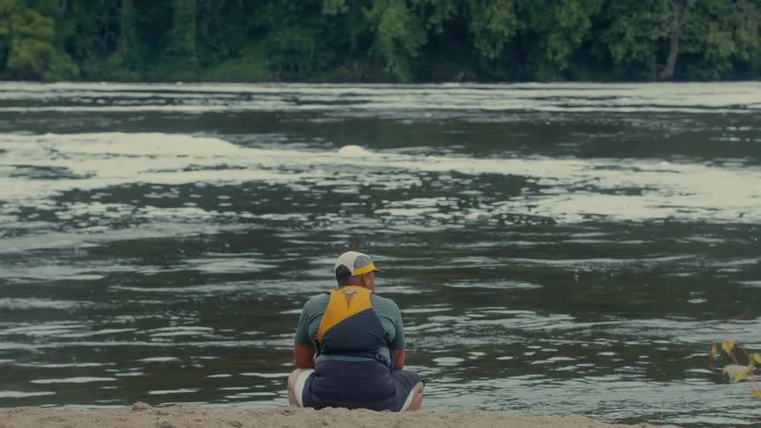 Person in life jacket sitting on the bank of a river