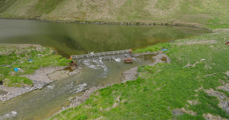 Water flows down a river that sits in a rural area of grass and hills