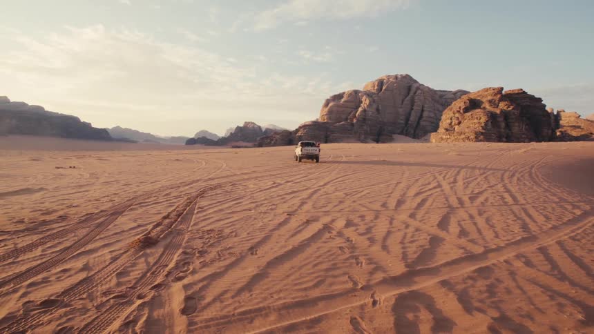 A rugged truck drives across a vast sandy desert landscape