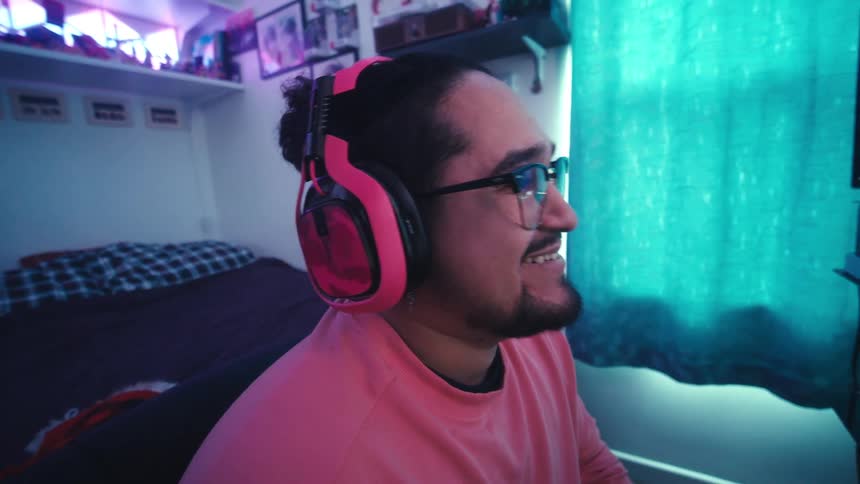 A man wearing pink headphones and sweater playing video games in a colorful bedroom