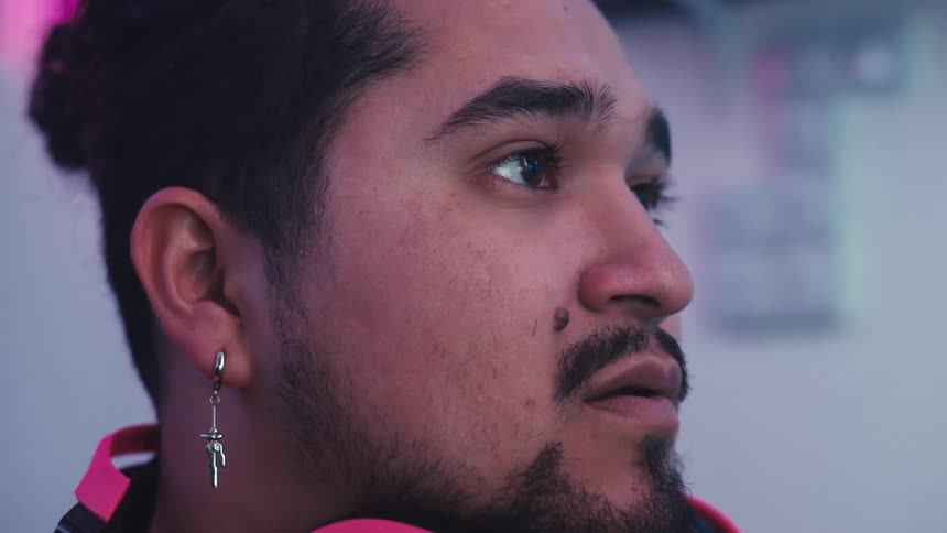 Closeup of a mans face wearing pink headphones around his neck and a bright earring