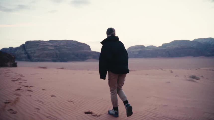 Woman climbing a sand hill in a natural environment surrounded by mountains