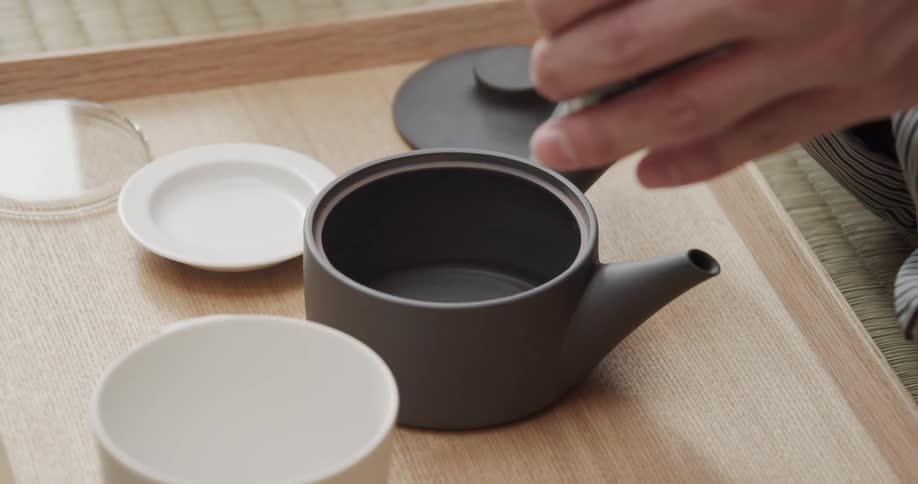A person is preparing matcha tea using a bamboo whisk to stir powdered green tea