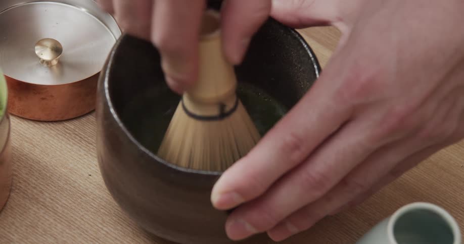 A person whisks matcha powder in a bowl using a bamboo whisk