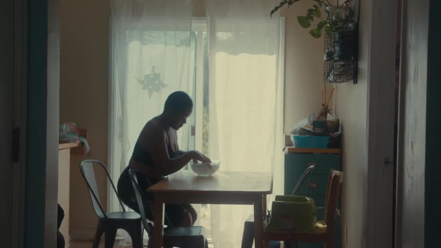 A woman sits at a table in a dimly lit room gently placing her fingertips into a bowl filled with ice water