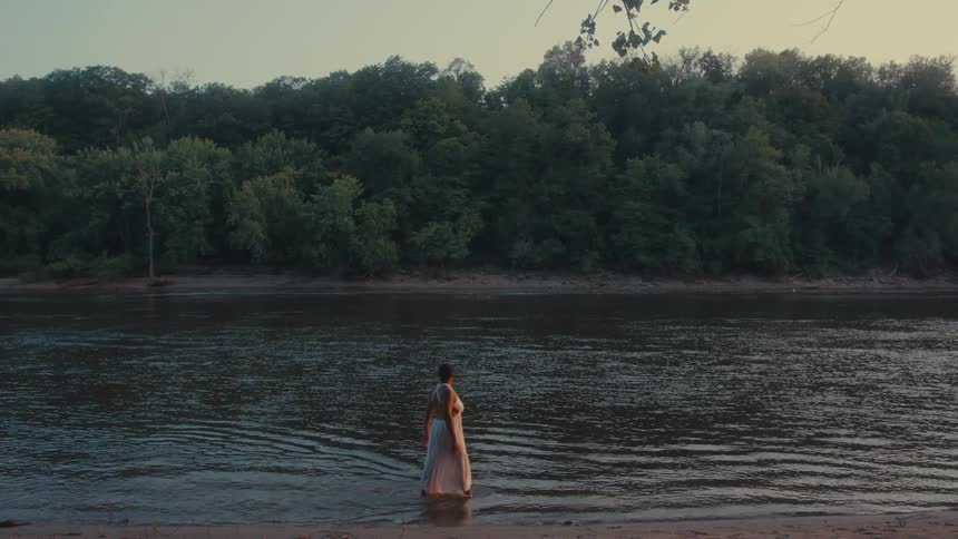 A woman on a white dress walking on the shallow waters of a river
