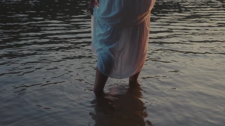 A person wearing a white dress is standing kneedeep in calm rippling water