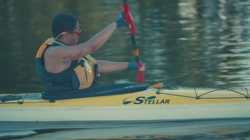 A person is kayaking on a calm body of water using a doublebladed paddle to propel a yellow kayak forward