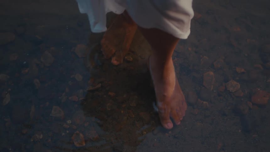 Bare feet walk through shallow water creating ripples