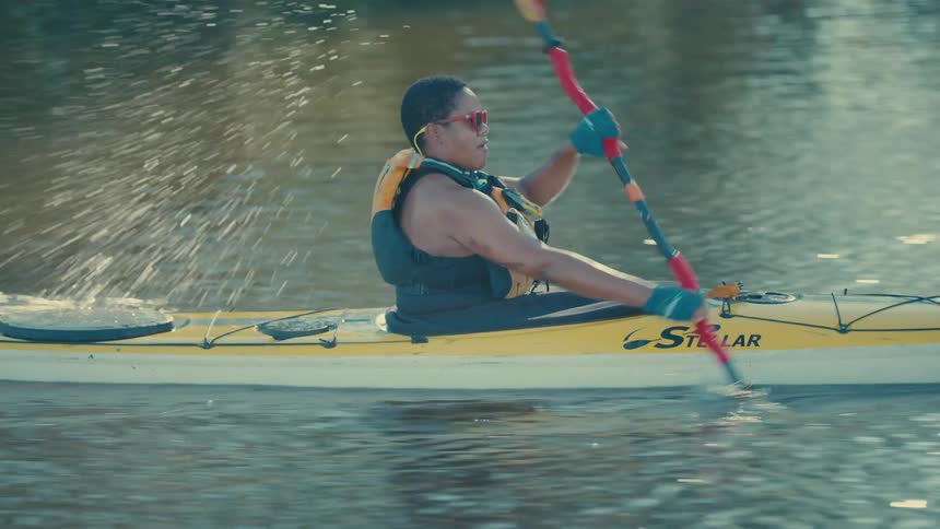 A person is kayaking on a calm river paddling a yellow kayak