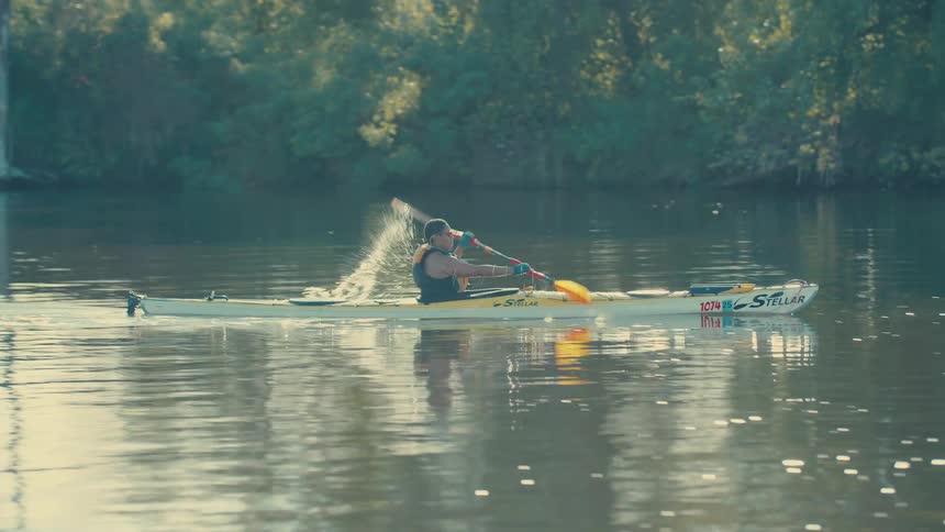 A woman in a canoe uses oars to row in a lake