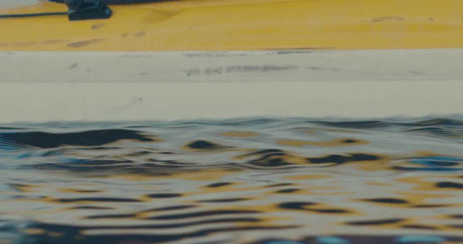 A yellow kayak glides through choppy water leaving a foamy wake in its path
