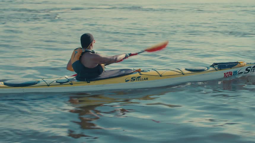 A person is kayaking on a calm body of water using a doublebladed paddle to propel a yellow kayak forward