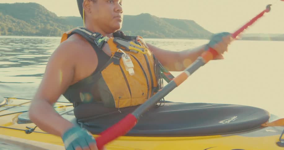 A person is kayaking on a calm body of water using a doublebladed paddle to propel a yellow kayak forward