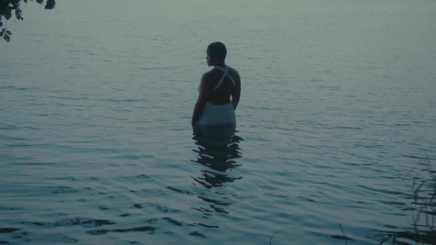 A woman wearing a bathing suit stands still in a lake and looks up