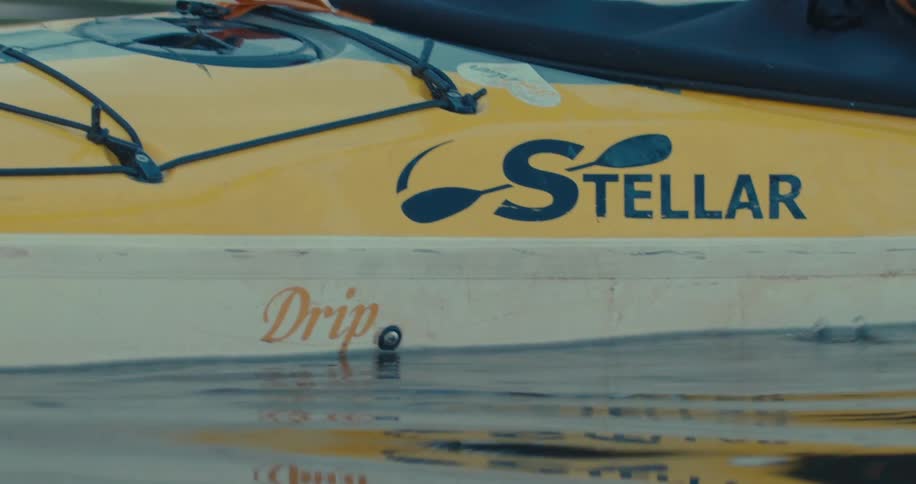A yellow kayak with the word stellar emblazoned on its side gliding through calm water with a paddle dipped in the water