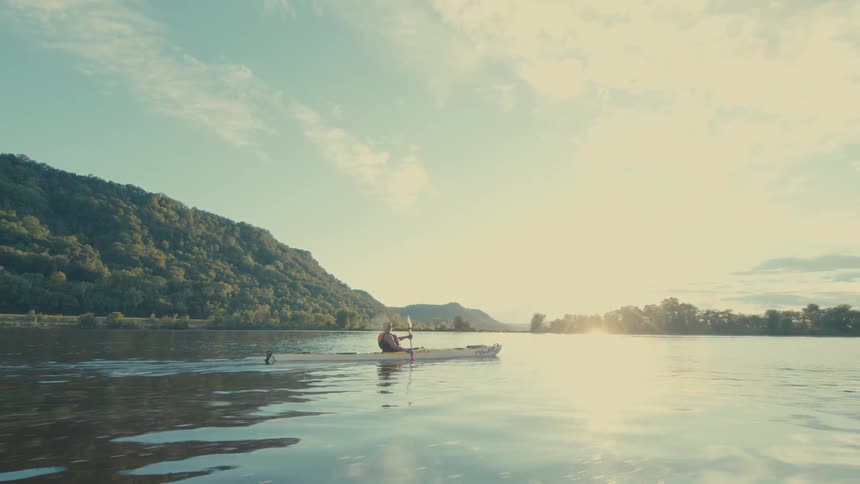 A person is kayaking on a calm body of water using a doublebladed paddle to propel a yellow kayak forward