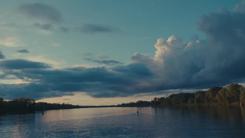 A lone kayaker paddles across a river at dusk silhouetted against a sky ablaze with vibrant hues of orange and purple