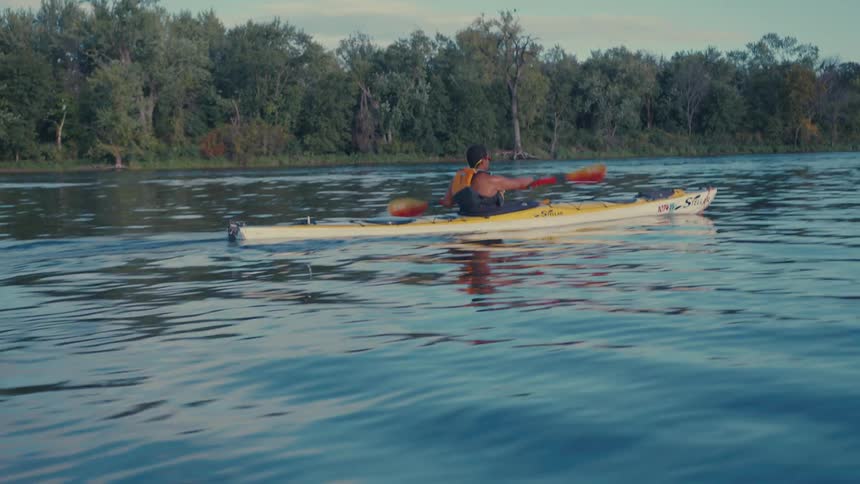 A person is kayaking on a calm body of water using a doublebladed paddle to propel a yellow kayak forward