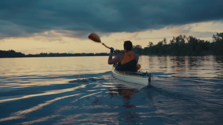 Man is kayaking on a body of water while the sun is setting