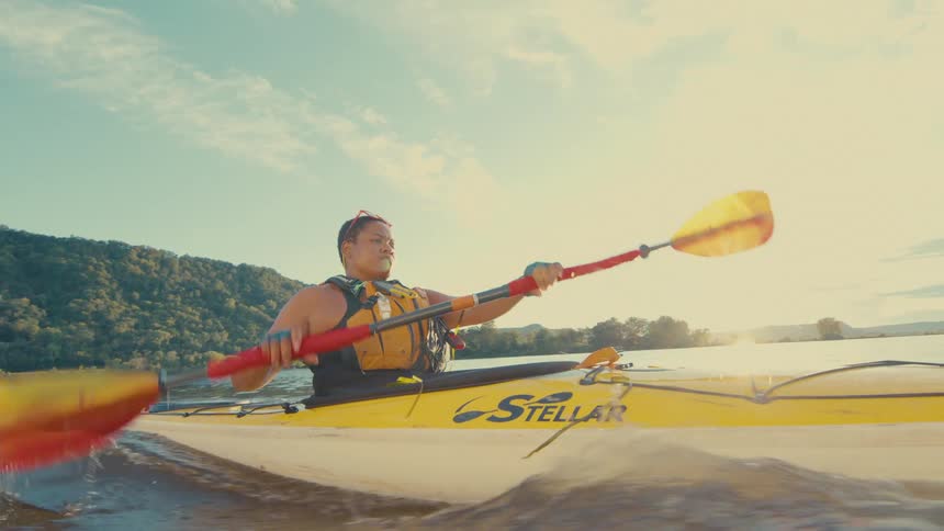 A woman uses an oar to move a kayak across a lake