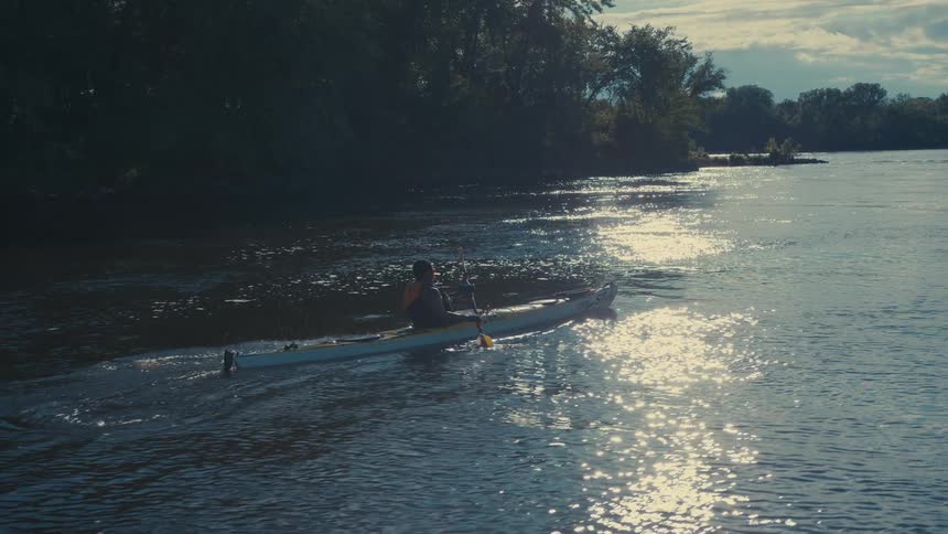 A woman in a canoe uses an oar to proceed down a lake