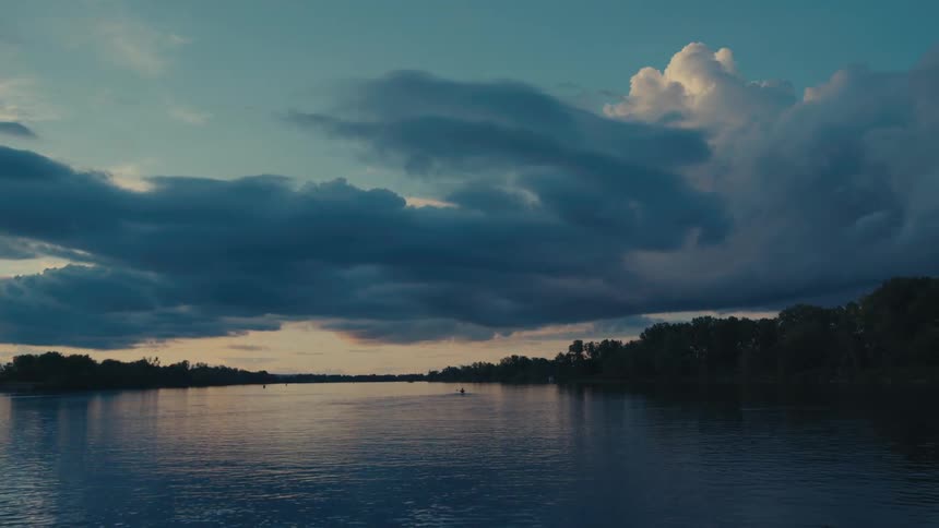 A lone kayaker paddles across a river at dusk silhouetted against a sky ablaze with vibrant hues of orange and purple