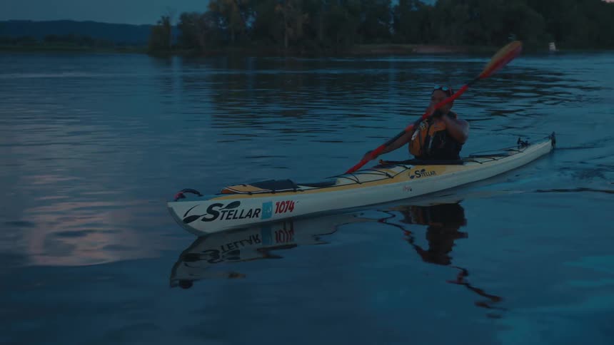 A woman is kayaking on a calm lake during twilight