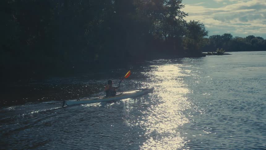 A person is kayaking on a calm body of water using a doublebladed paddle to propel a yellow kayak forward
