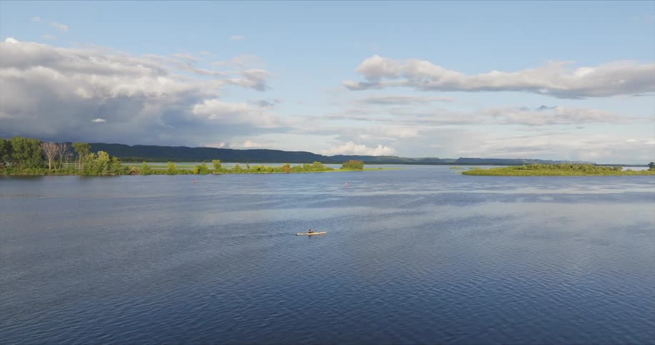 Aerial view of a single person canoeing on a large lake with mountains on the horizon