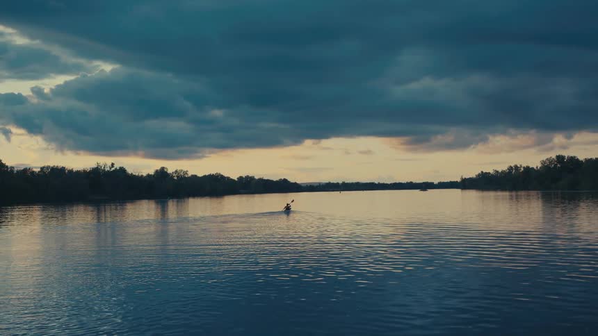 Silhouette of a person canoeing on a calm river on a cloudy day