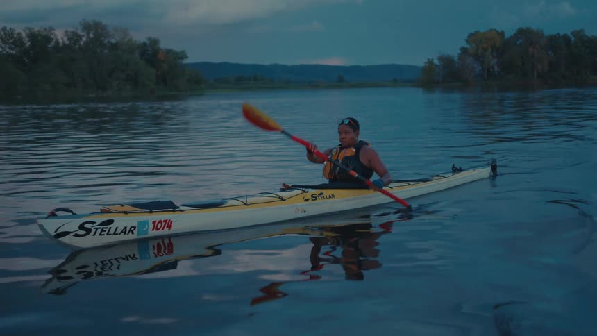 Person paddling a canoe in the middle of a river at dawn