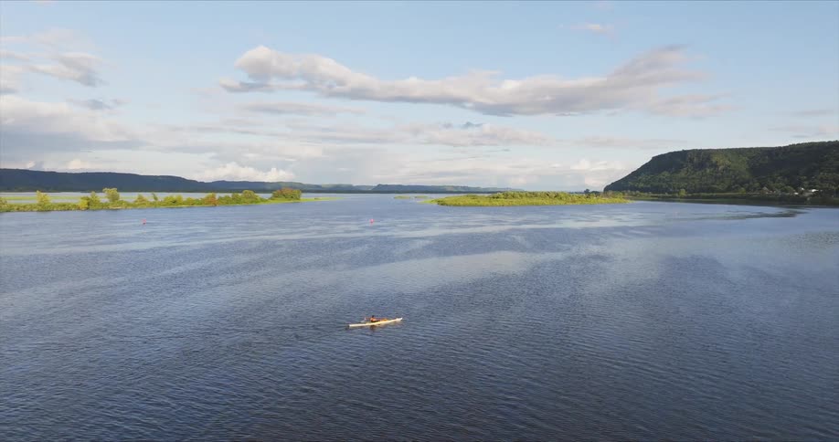 Person paddles a kayak far from the mountainous shore on a cloudy day