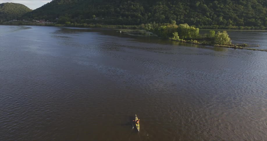 An aerial view of a person kayaking on a large body of water with a forested shoreline and a small island