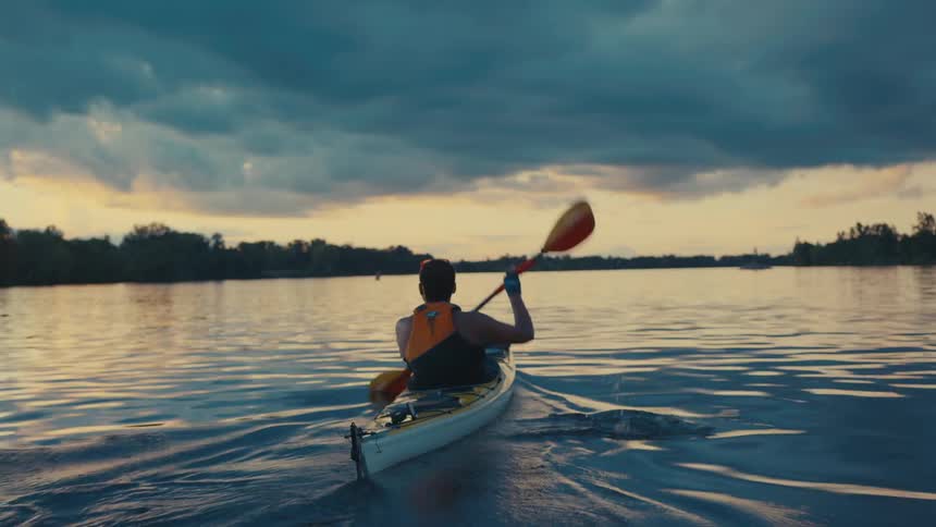 Person paddles a kayak on the river near dawn on a cloudy day