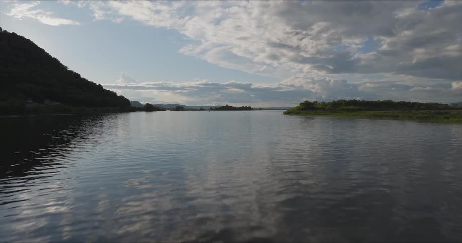 The tranquil river its surface rippling with gentle waves reflects the vibrant hues of the sky as it flows through a landscape of rolling hills and distant shores