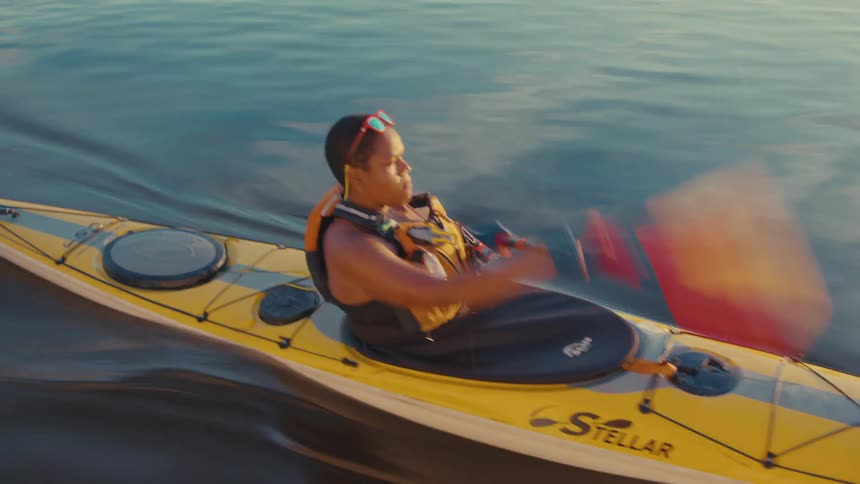 A woman paddles her yellow kayak on smooth water