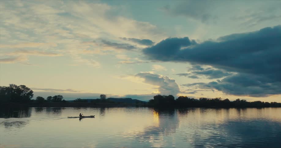 Silhouette of a person canoeing on a river at dawn