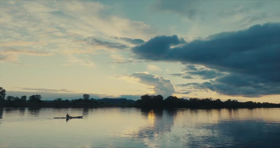 A lone kayaker glides across a tranquil lake at sunset casting a long shadow on the waters glassy surface