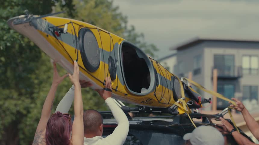 Several people attempt to mount a kayak on top of a vehicle in a neighborhood