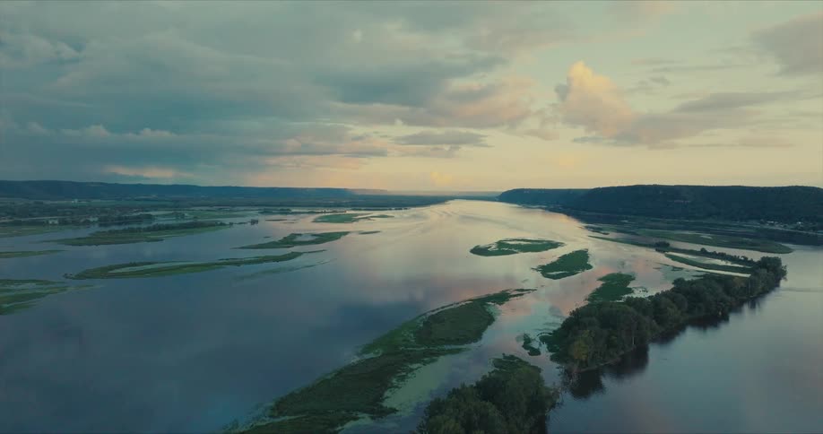 Aerial view of a river winding through a landscape with lush green islands and peninsulas under a sky filled clouds during sunset