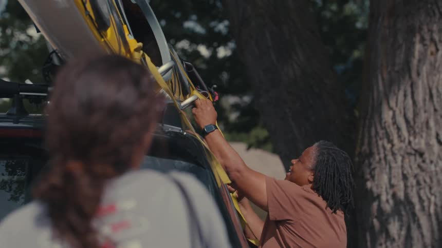 A woman untying a rope that is learning a kayak that is on top of a car