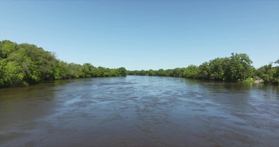 Calm river surrounded by vegetation against a clear blue sky